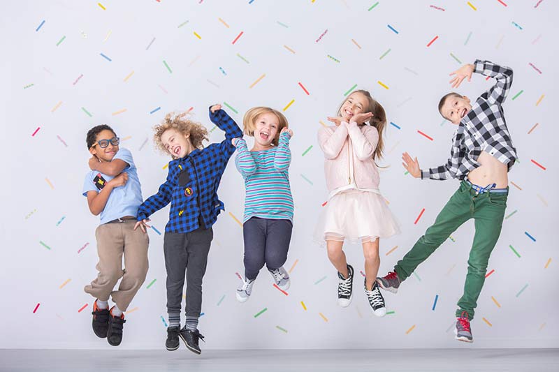 Eine fröhliche Gruppe von Kindern springt vor einer bunten Wand in die Luft